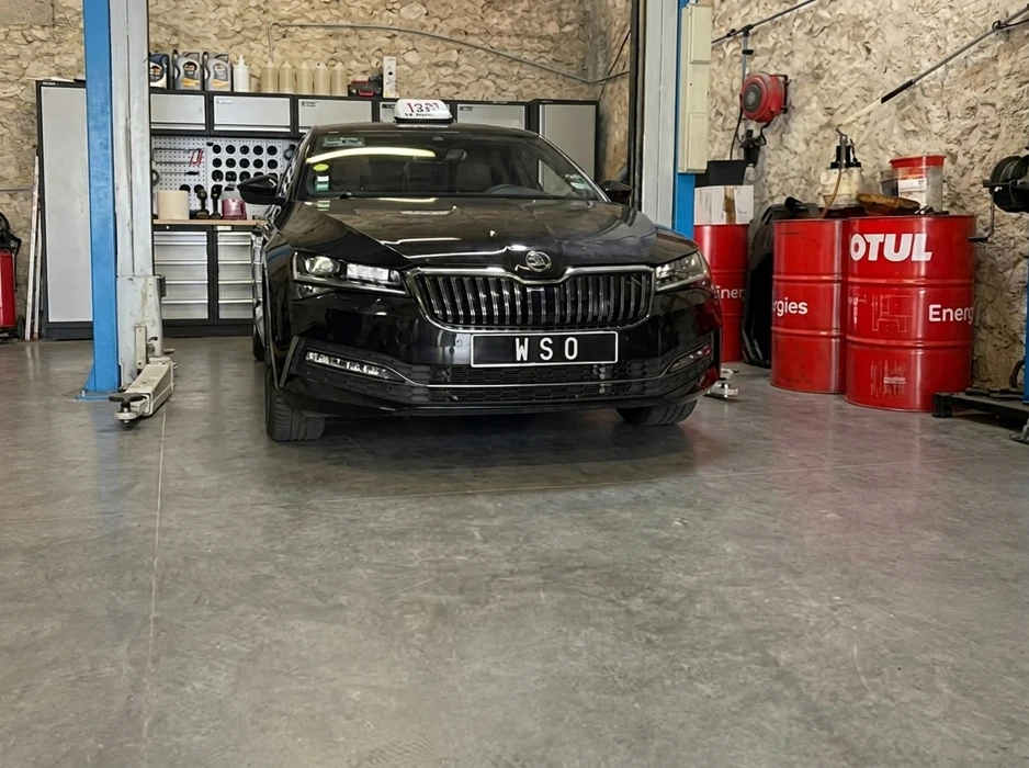Garage automobile intérieur, une Škoda Superb noire (3ème génération) immatriculée "WSO" est positionnée sur des chariots de déplacement