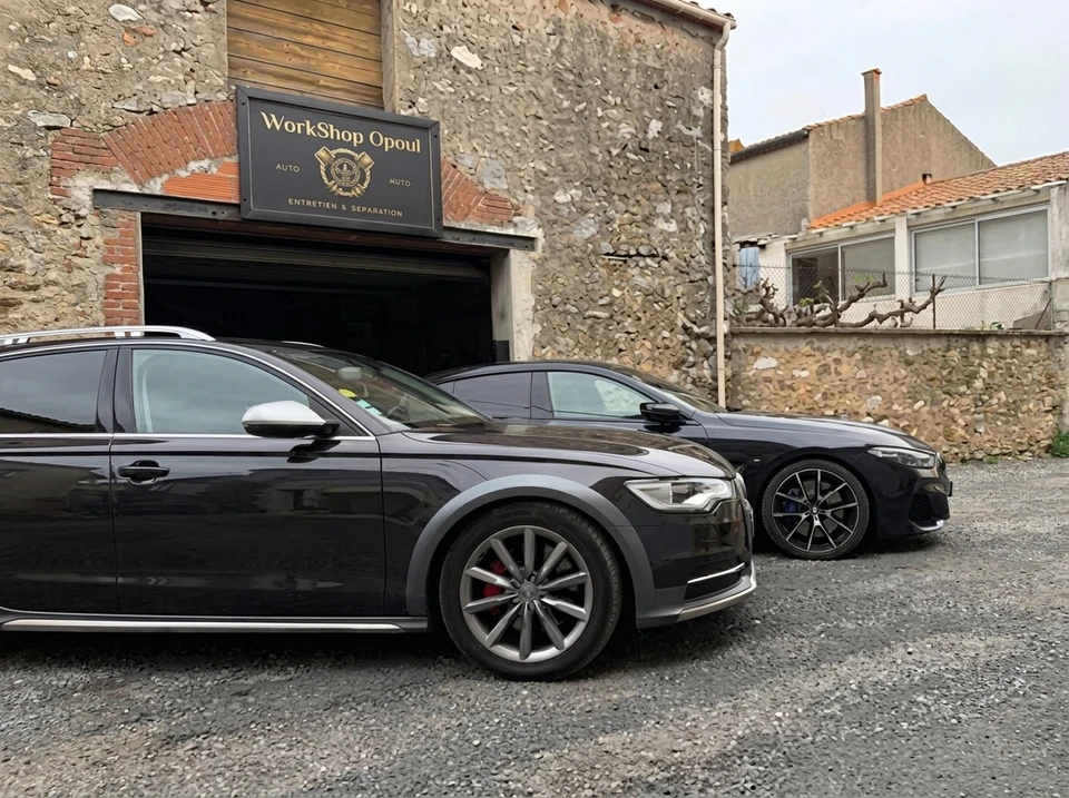 Deux véhicules noirs garés devant l'atelier "WorkShop Opoul" en pierre apparente